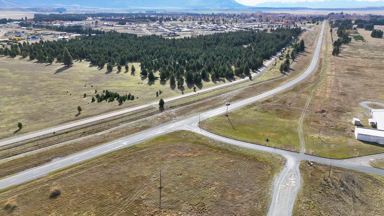 Drone footage captures a scenic road through a rural landscape with trees and open fields under clear skies