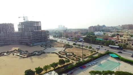 aerial tilting up view of a highway of the city with traffic going on, under constructed building with crane of its top, a sports area and empty plot with its roads