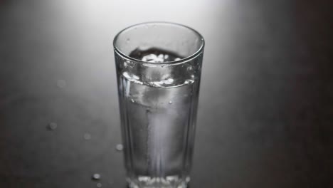 cube of ice falls into glass tumble of waterr in slow motion