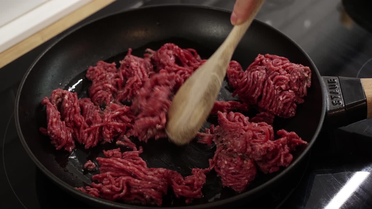 Frozen raw minced beef in frying pan with wooden spoon preparing for cooking stage