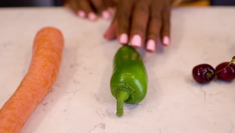 la mano de una mujer negra está agarrando seductoramente verduras de pimienta verde en una mesa de cocina de mármol
