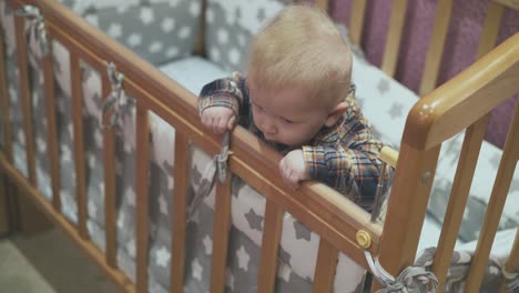 little baby leans on wooden cot with soft linen at home