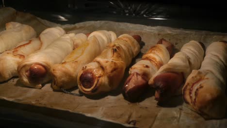 sausages in the dough are getting baked in an oven