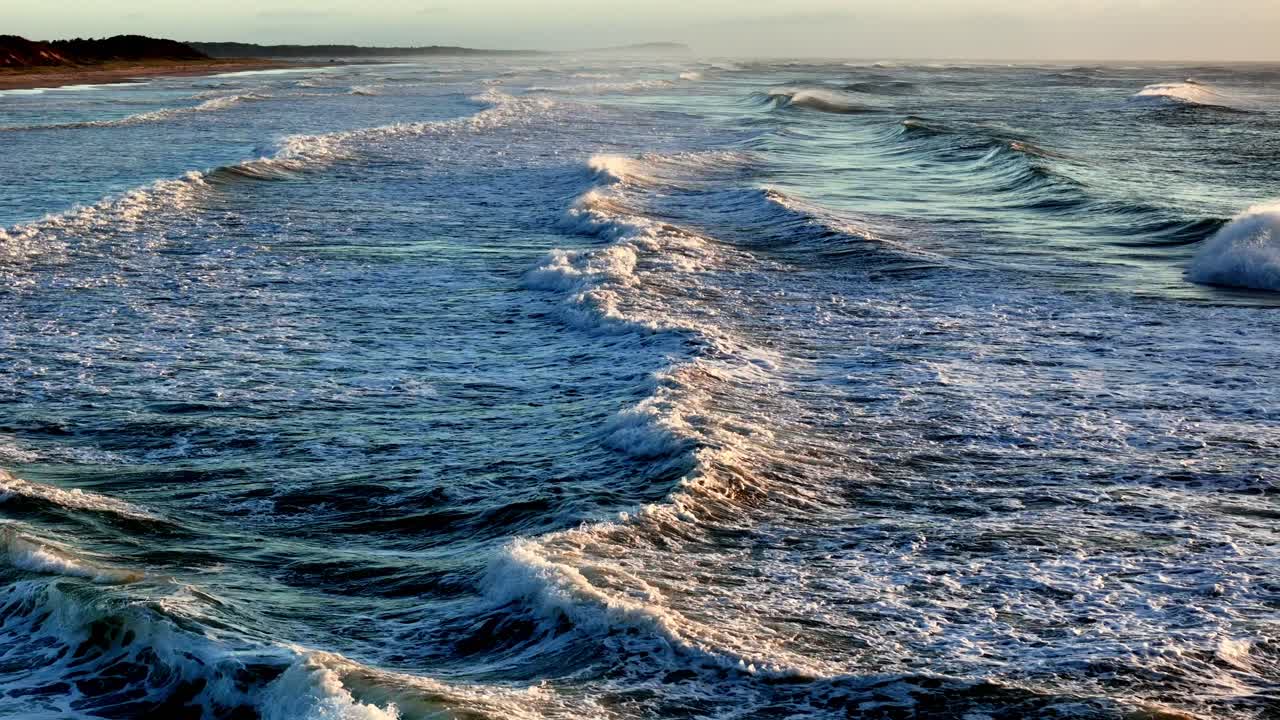 Aerial view of the foamy waves crashing against the shoreline, Sunlight casting a golden glow on the ocean's froth
