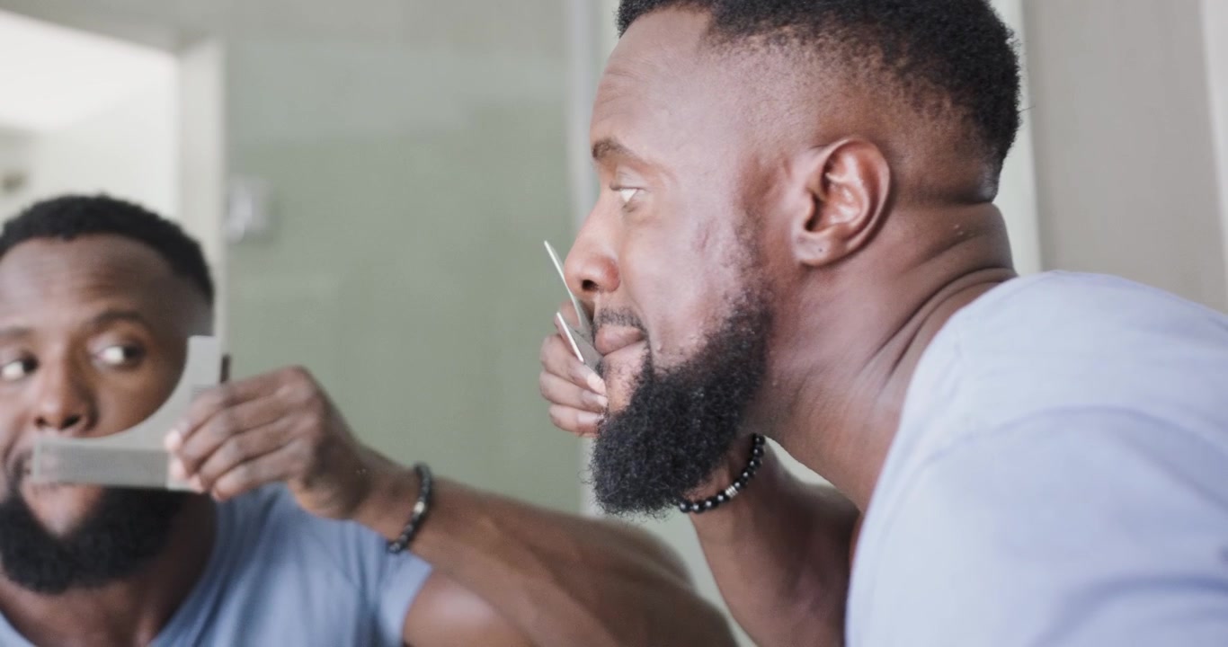 Uomo africano che tiene uno stencil curvo per barba, allineando e rifinendo con un rasoio allo specchio per un bordo preciso.