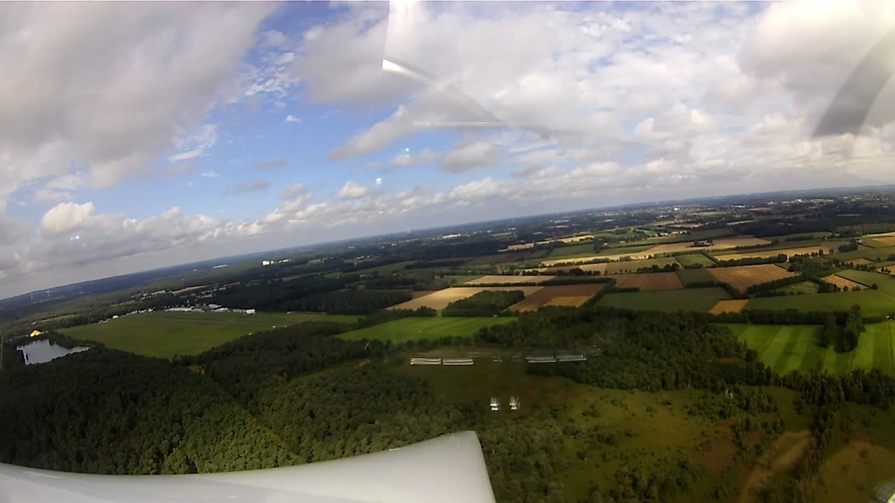 Wing of a glider over a green landscape in fine weather sky with clouds