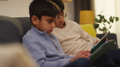 two young boys sitting on sofa at home playing games or streaming onto digital tablets 21