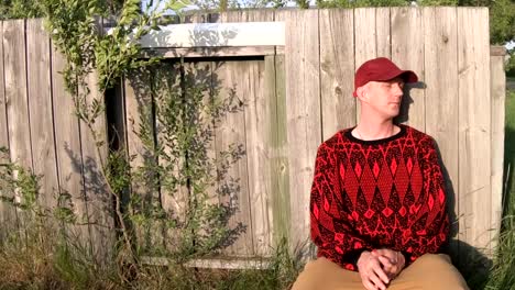 Male-adult-wearing-a-black-and-red-sweater-against-a-fencewreating-in-the-sun.