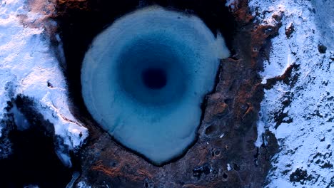 aerial view of a drone which getting further and further of the center of a geuser in geysir, iceland . smoke is getting out of the geyser with people walking all around the geyser, under the red sunset.