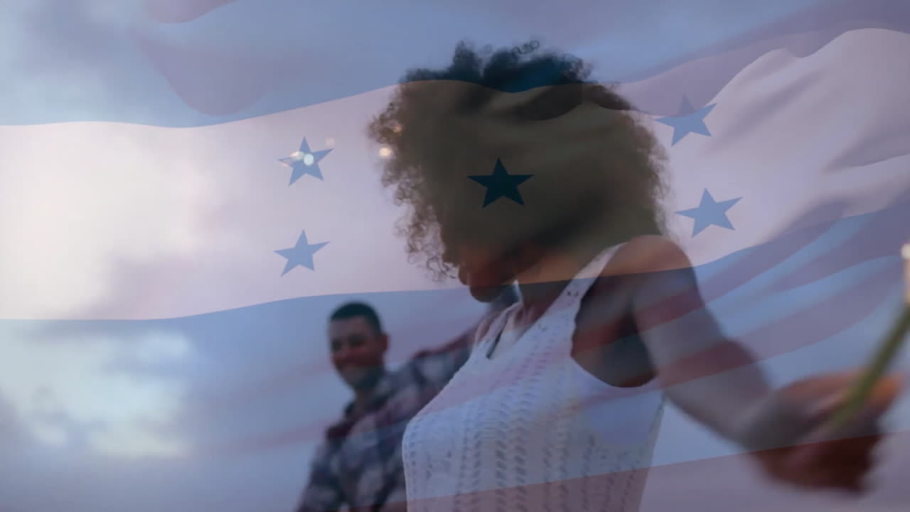 Animazione della bandiera dell'Honduras su una coppia felice e diversificata che balla con stelle filanti sulla spiaggia al tramonto