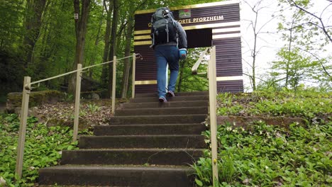 Excursionista-Masculino-Pasando-Por-La-Puerta-Simbólica-En-La-Ciudad-De-Pforzheim-Iniciando-El-Popular-Sendero-De-Larga-Distancia-Westweg-A-Través-Del-Bosque-Negro-En-El-Sur-De-Alemania