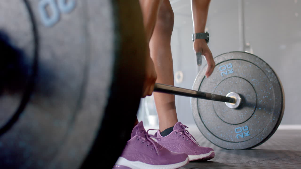 Lifting barbell, woman in gym wearing purple sneakers, focusing on workout
