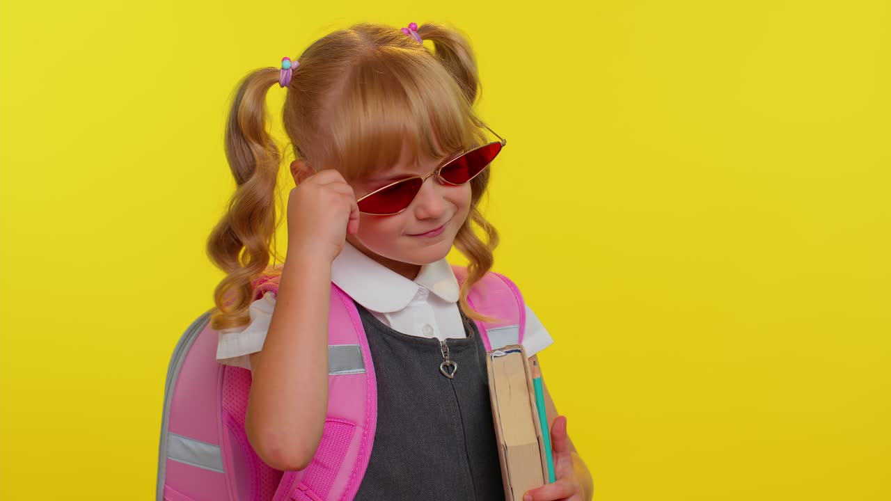 Hübsches, süßes Teenager-Mädchen in Schuluniform und Sonnenbrille zwinkert und blickt lächelnd in die Kamera