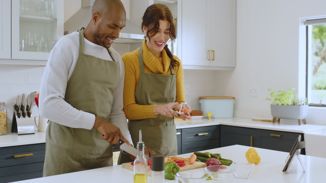 Diverse multiracial couple cooking together in modern kitchen, smiling and enjoying moment, at home