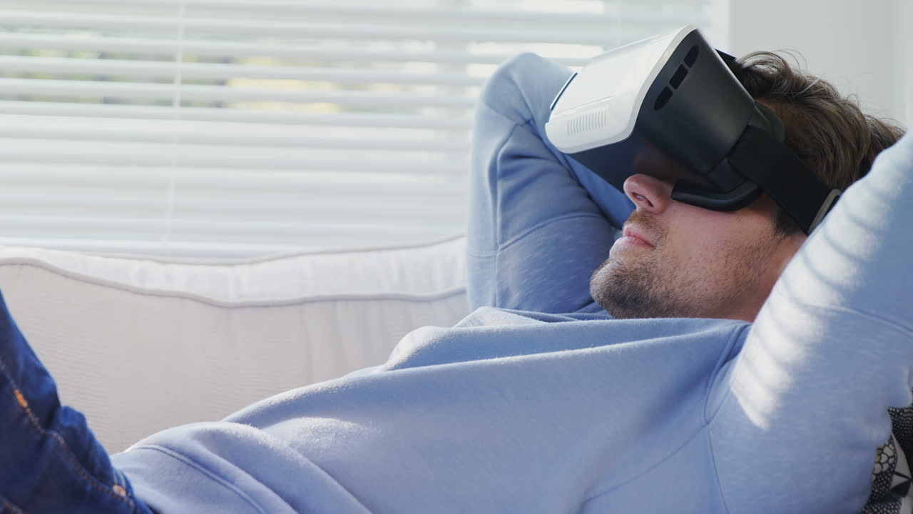Young man lying on sofa wearing virtual reality headset at  home 4K 4k