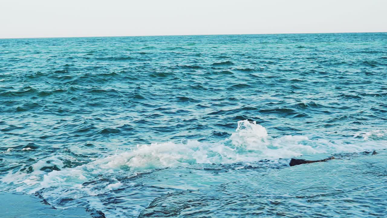 Crests of the waves are breaking on the reefs near the shore in the summer. Seascape. Slow motion. Aerial view