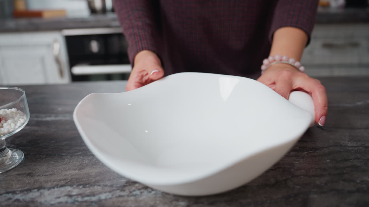 vista parcial de la mujer girando sosteniendo un cuenco blanco, colocándolo suavemente sobre la mesa, deja caer cuidadosamente huevos en el mostrador con su mano adornada con una pulsera