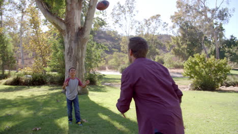 un niño y su padre jugando al fútbol americano en un parque.