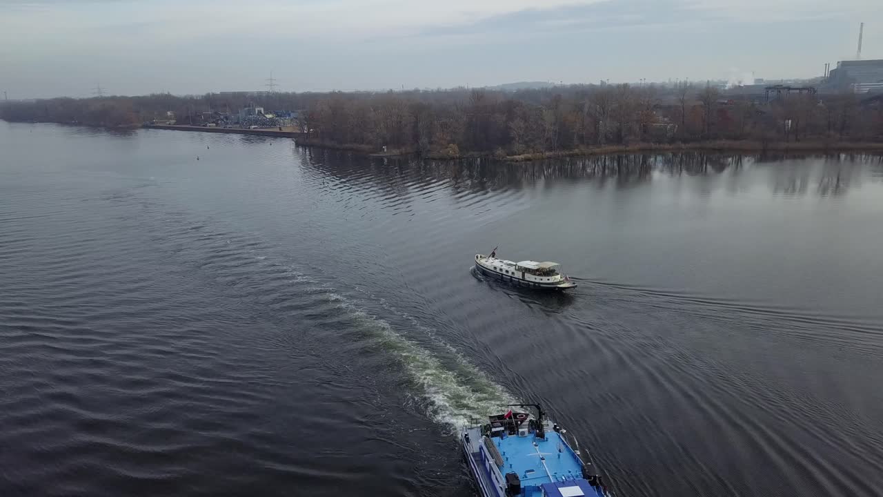 Vue aérienne panoramique vers la gauche d'un bateau de passagers naviguant sur les eaux calmes de l'Elbe Labe, entouré d'une forêt automnale et d'une légère brume matinale