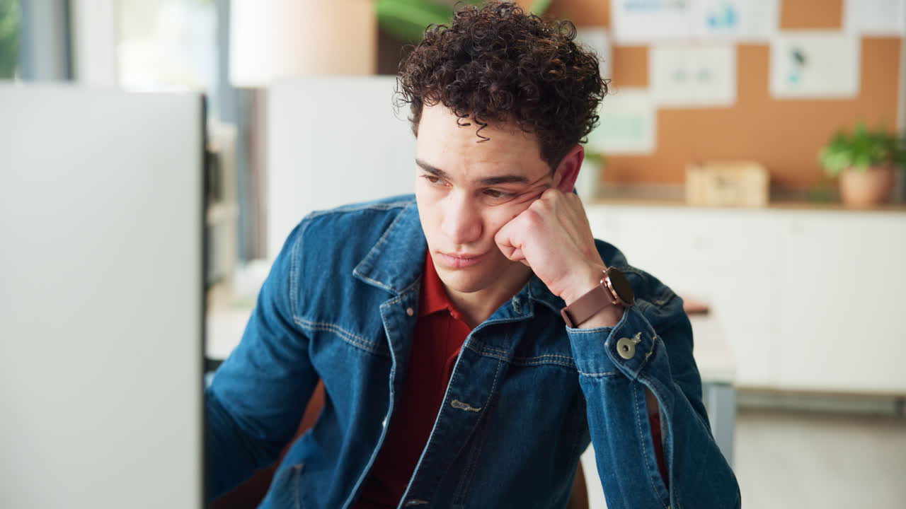 Giovane uomo stanco che guarda lo schermo del computer in ufficio