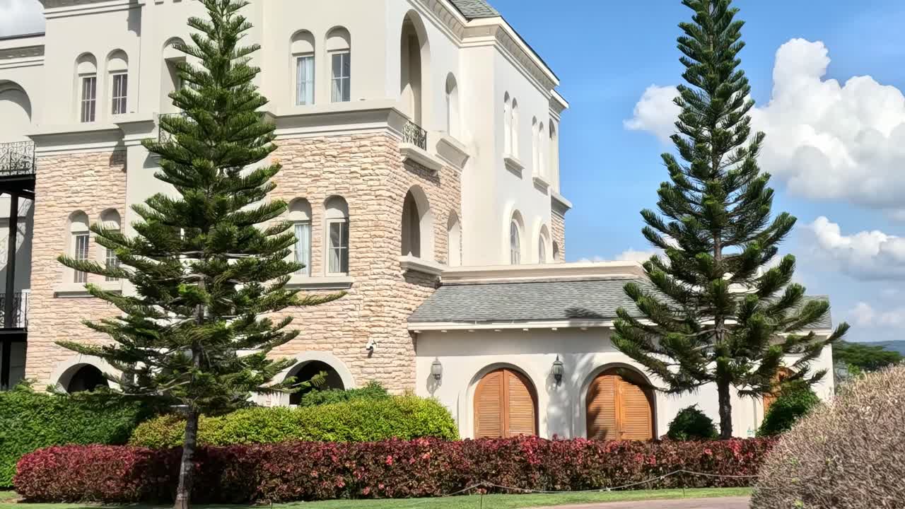 A detailed view of a castle's facade, featuring arched windows, stone walls, and surrounding greenery.
