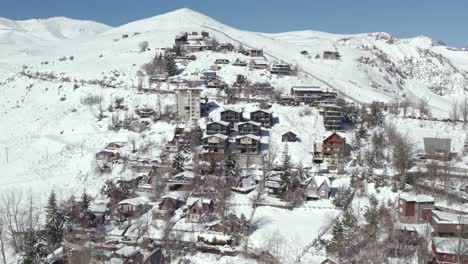 órbita aérea estableciendo el pueblo montañoso de farellones lleno de nieve en la temporada de invierno, efecto de paralaje con la cordillera de los andes y la estación de esquí el colorado, chile