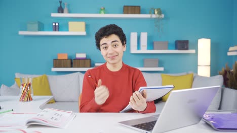 Feliz-Estudiante-Varón-Estudiando-En-El-Escritorio-Y-Sonriendo-A-La-Cámara-Y-Expresando-Feliz-Estudio.