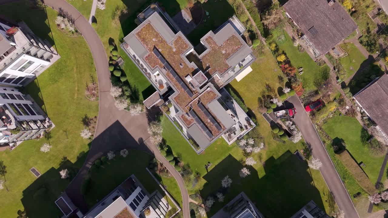 Aerial top down shot of green vegetated rooftop with solar panels on sunny day. Modern multi-family residential house in swiss city. Descend shot.