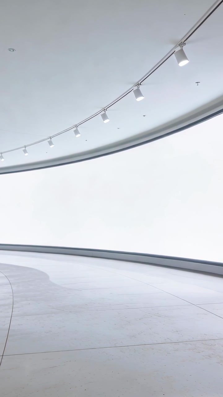 Vertical video: Tilting camera panning right highlighting curved white wall, gallery floor, lights