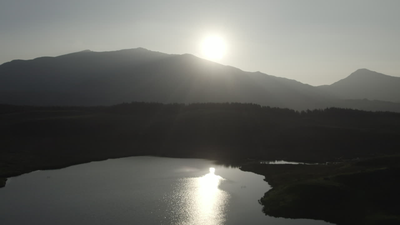 Drone sideways flight across Llyn y Dywarchen lake at sunrise with Snowdon mountain in the background. Aerial footage captures morning light over water and scenic North Wales countryside landscape