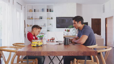 Hispanic-father-and-son-working-opposite-each-other-at-the-dining-room-table,-side-view,-close-up