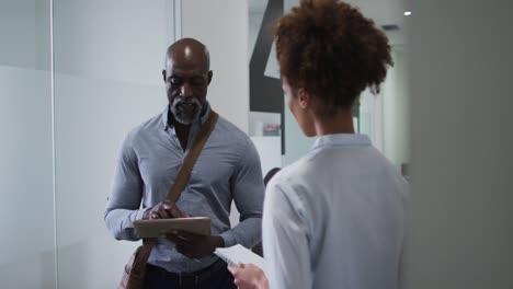 Diverse-male-and-female-business-colleagues-talking,-man-using-digital-tablet-in-office-corridor