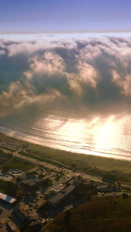 huge wave of thick white fog moving from the ocean to the beach. little residential area at the coastline of montara, california, usa from aerial perspective. vertical video