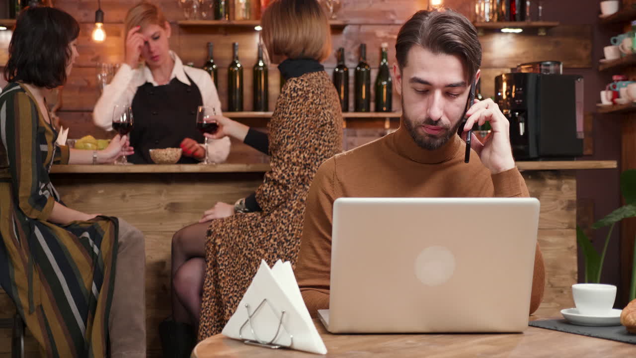 Man working on laptop while people drink wine at a cafe