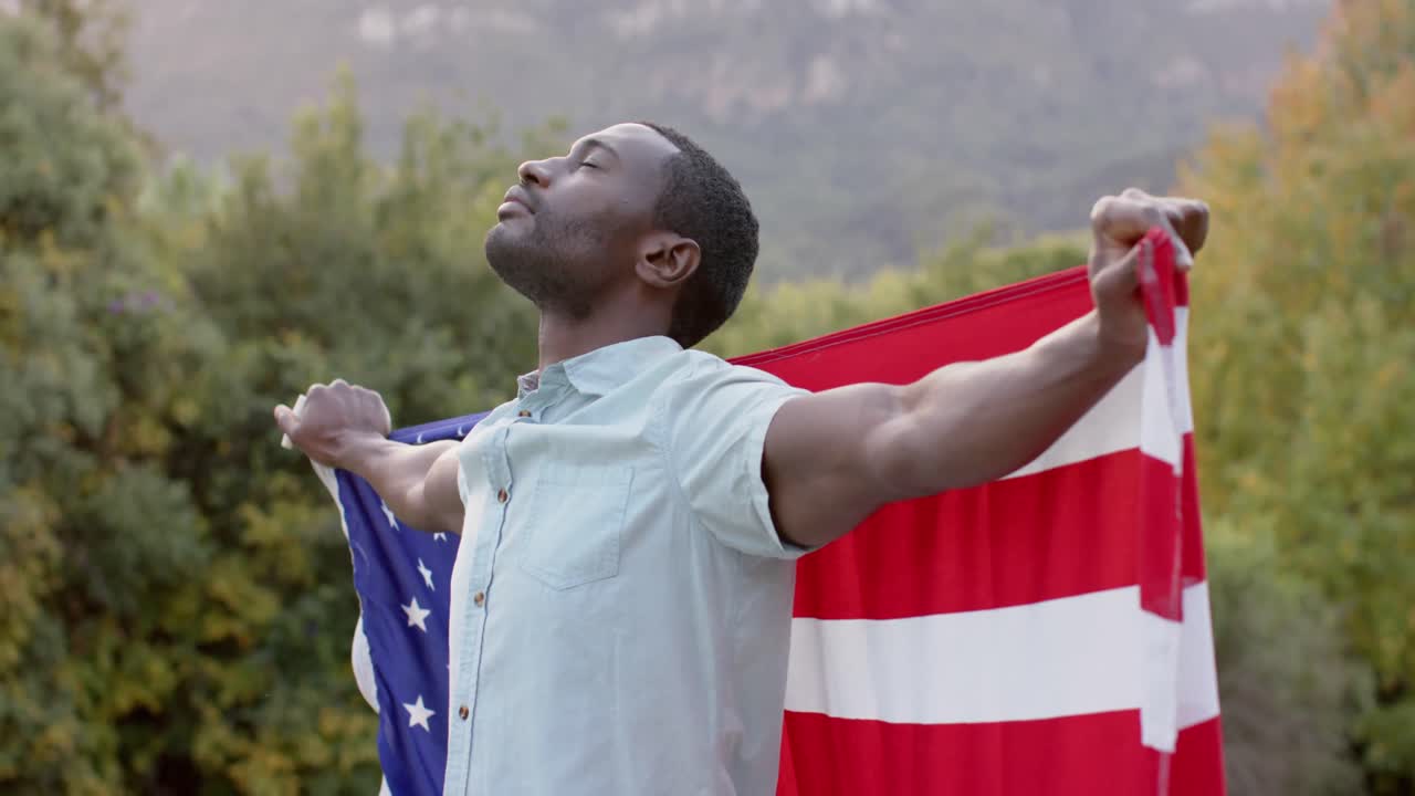 Portrait d'un homme afro-américain tenant un drapeau des États-Unis dans un jardin, au ralenti.