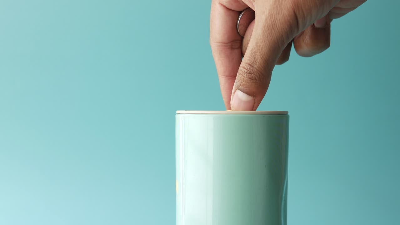 손으로 동전을 밝은 푸른색 돼지 은행에 넣는 것