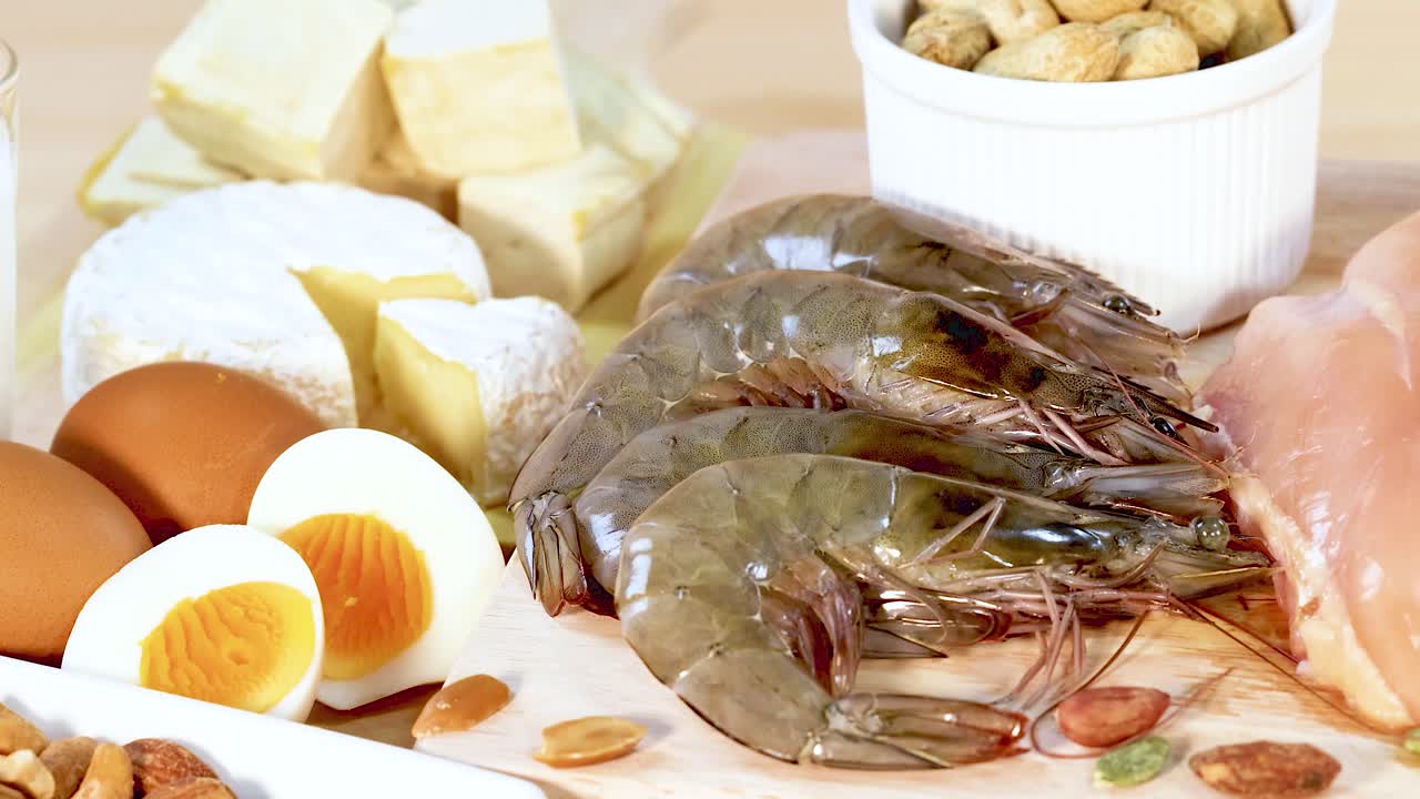 una variedad de alimentos ricos en proteínas, incluidos nueces, huevos, mariscos y lácteos, están artísticamente dispuestos en una superficie de madera