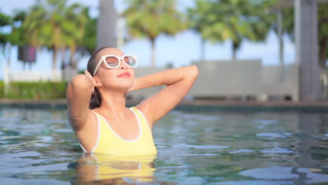 primer plano de una mujer en una piscina alisando su cabello húmedo hacia atrás lejos de su cara
