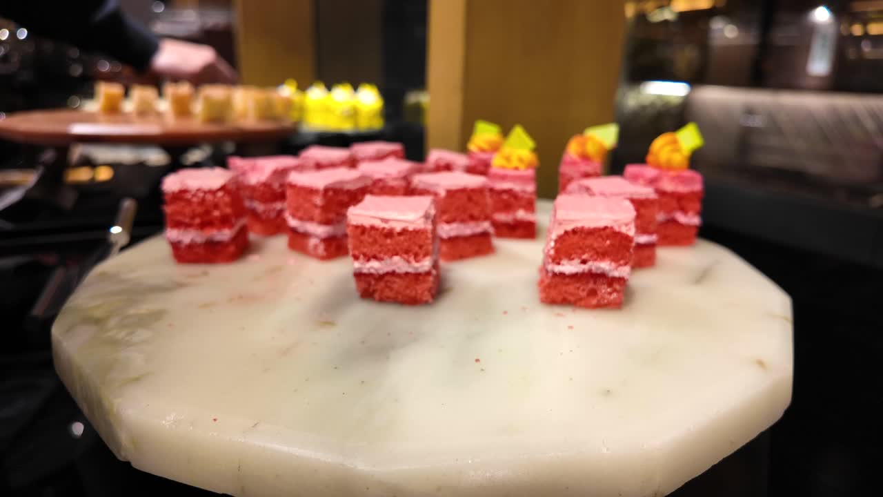 Pink and red mini cakes on a dessert buffet with serving tongs