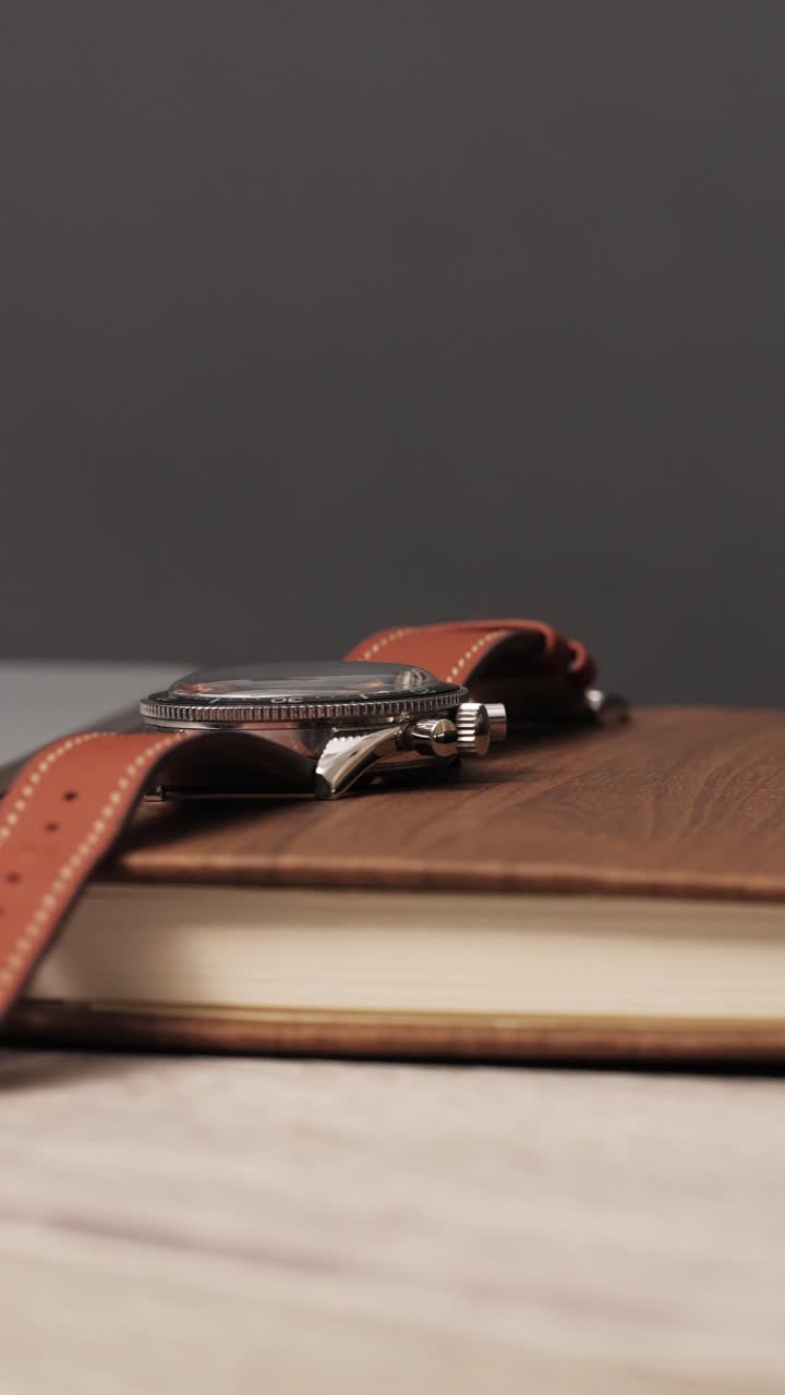 A slow rotation reveals a luxury wristwatch resting on a notebook with a pen, evoking a business and productivity theme