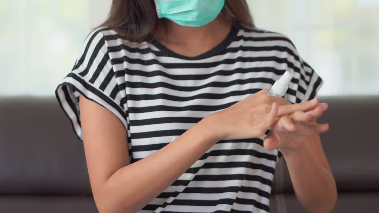 Una donna con una mascherina spraya del disinfettante sulle mani e poi lo strofina energicamente
