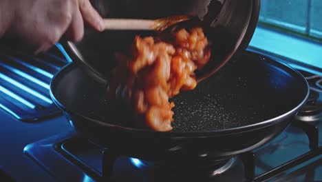 mans hands transferring sliced chicken breast pieces from a bowl with a wooden spoon onto a hot skillet, then holding the pan and spreading evenly