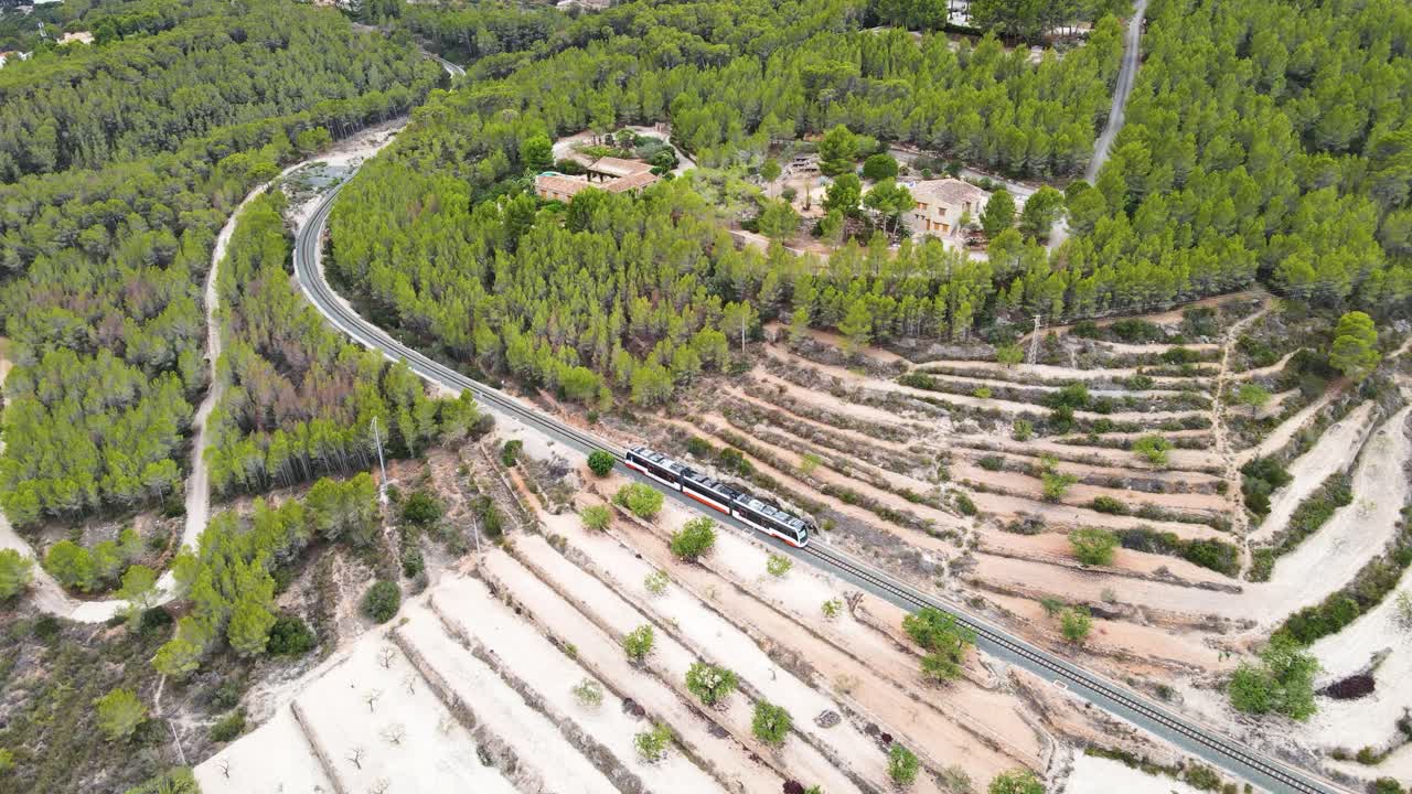 Train passing through green hills and terraced fields near Calpe Spain, aerial view