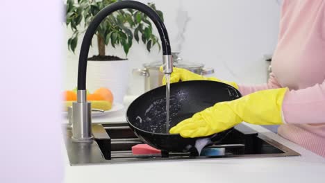 a woman in yellow gloves washes a pan