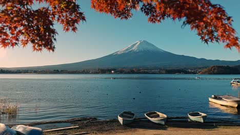 una vista serena del monte fuji enmarcada por el vibrante follaje rojo de otoño en el lago kawaguchiko, japón. los patos nadan suavemente en primer plano, mientras que los pequeños barcos descansan en el fondo.