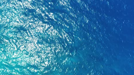 Drone-top-down-static-of-shimmering-light-across-blue-ocean-texture,-half-lit-by-sun