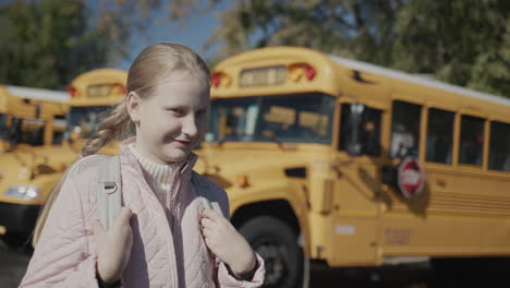 Portrait-of-a-schoolgirl-in-front-of-a-row-of-school-buses