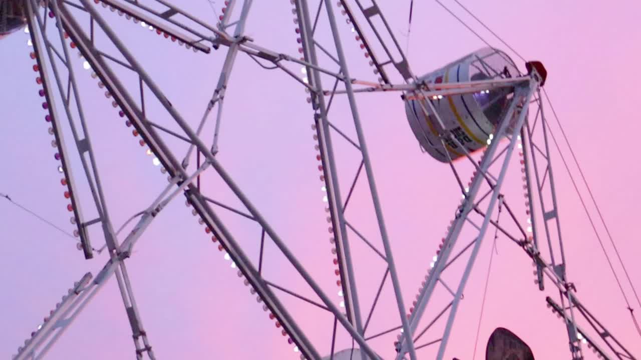 A small town ferris wheel spins as the camera pans right and stops at a water tower at dusk.