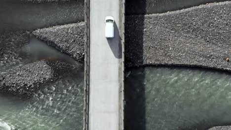 white car drives across bridge over meltwater river in iceland, aerial