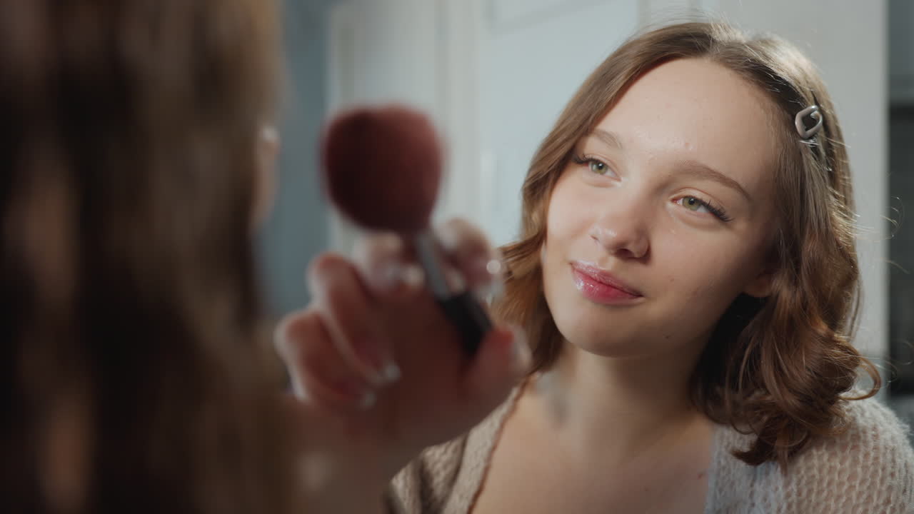 CloseUp Mirror Scene Showing Young Woman Watching As Apprentice Applies Blush, Hairclip Holds Curls Back, Soft Focused Expression, Training Atmosphere With Gentle Brush Strokes And Careful Technique